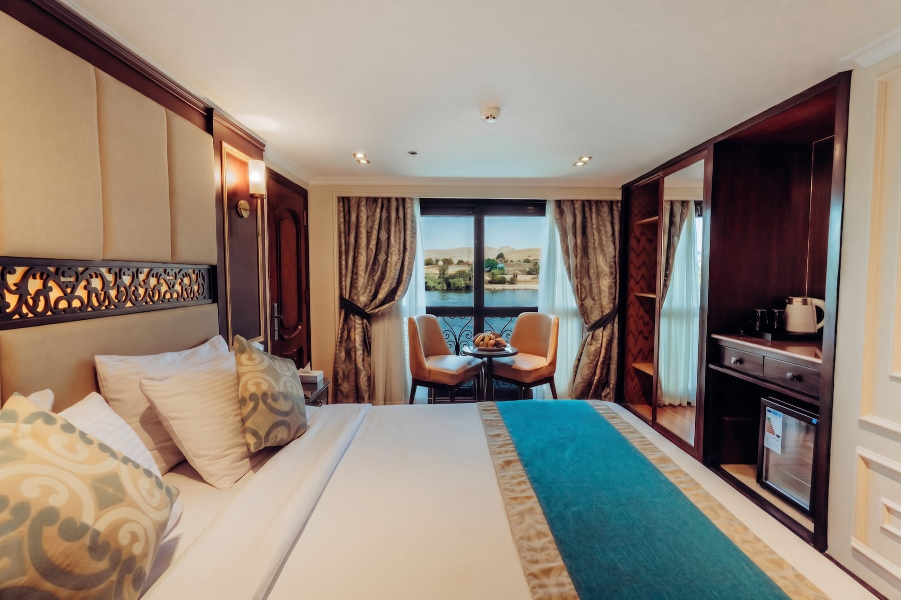 Elegante Kreuzfahrtkabine mit großem Bett, Sitzecke und französischem Balkon mit Blick auf den Nil.