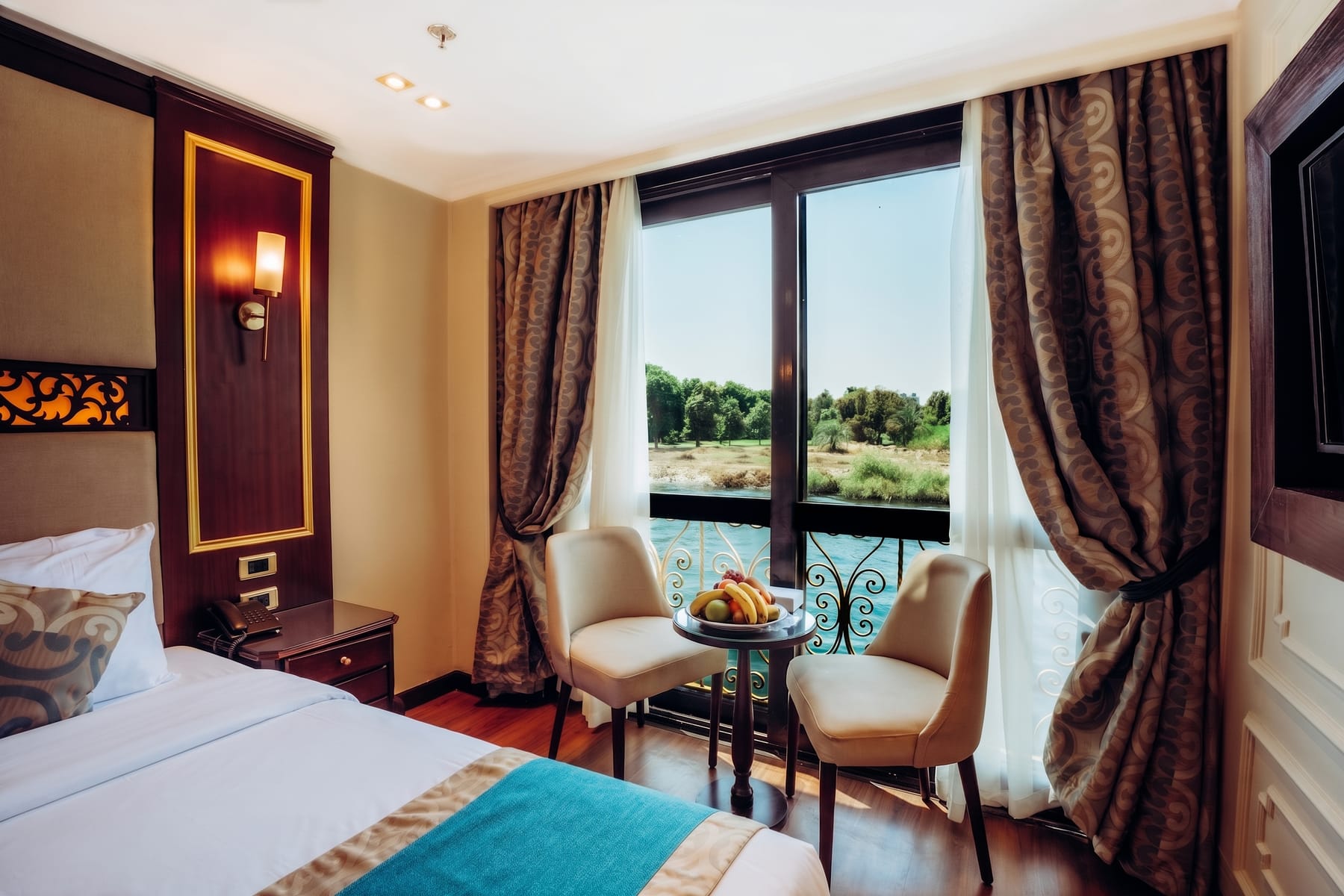 Elegant cruise cabin with a double bed, seating area, and French balcony overlooking the Nile.
