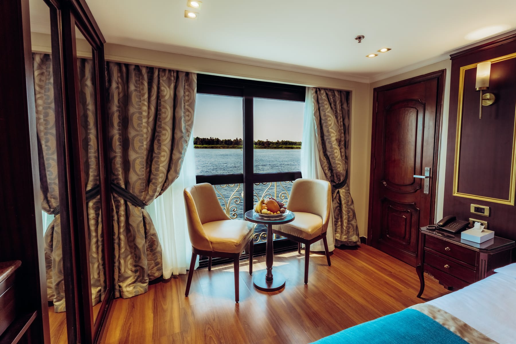 A ship cabin with seating area and French balcony overlooking the Nile River.