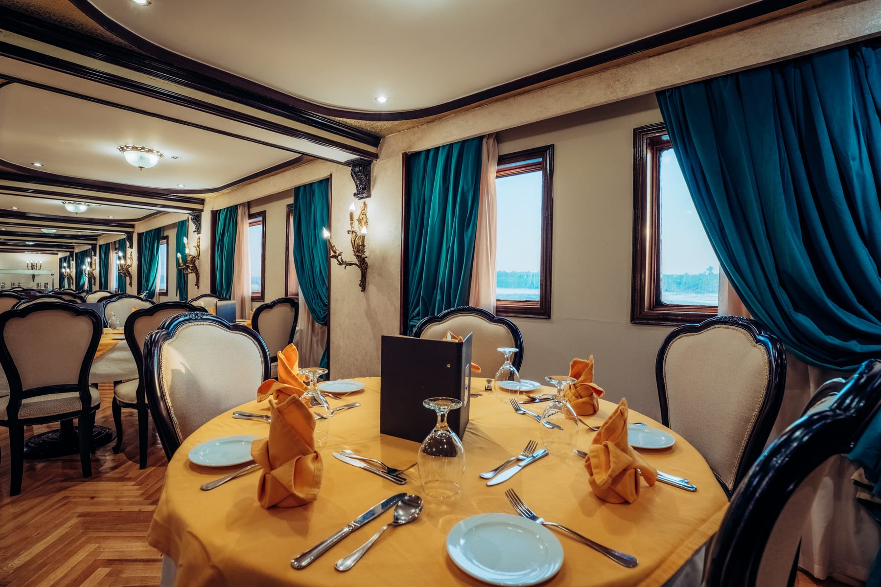Elegantes Restaurant an Bord der M/S City and Sea Adonis mit einem zum Essen gedeckten Tisch und Blick auf den Nil durch die Fenster.