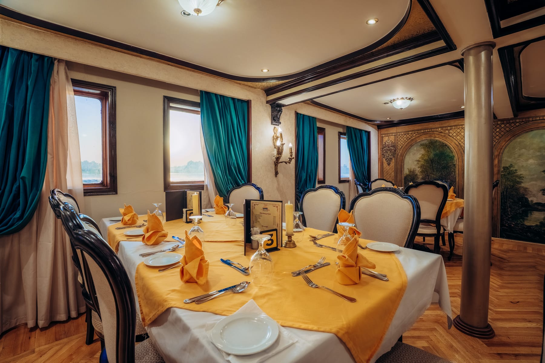 Eleganter Speisesaal an Bord der M/S City and Sea Adonis mit für eine Mahlzeit gedeckten Tischen und Blick auf den Nil durch die Fenster.
